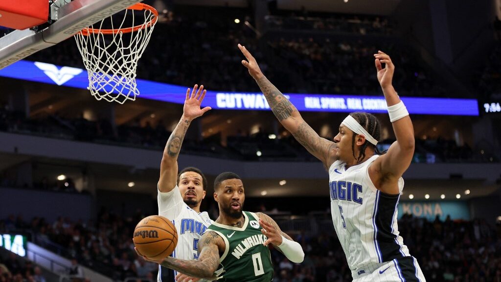 Damian-Lillard-0-of-the-Milwaukee-Bucks-is-defended-by-Cole-Anthony-50-and-Paolo-Banchero-5-of-the-Orlando-Magic-during-a-game-at-Fiserv-Forum-on-April-10-2024-aspect-ratio-16-9