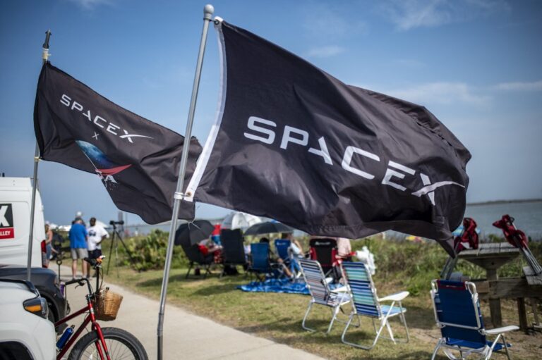 SpaceX flags fly as people wait on South Padre Island to watch the SpaceX Starship rocket launch from Starbase, Texas.