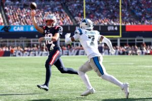 Drake Maye #10 of the New England Patriots throws the ball away under pressure from Tre'von Moehrig #7 of the Carolina Panthers
