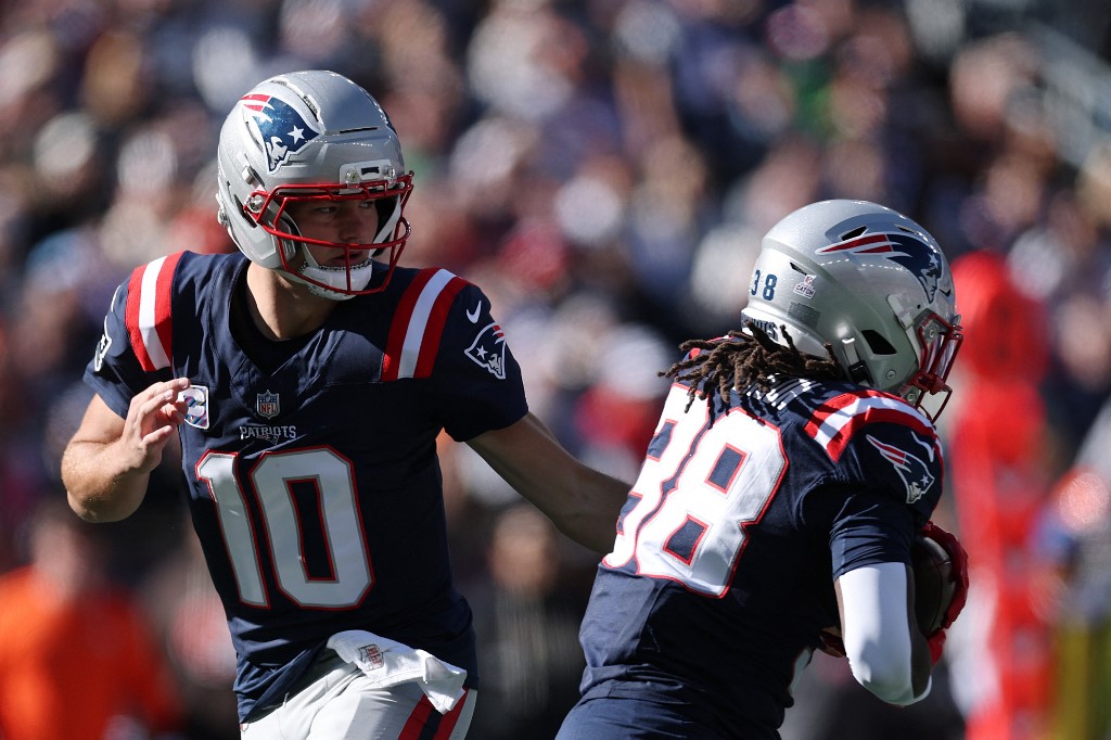 Drake Maye of the New England Patriots, one of the top candidates in our NFL MVP odds, hands the ball off to Rhamondre Stevenson #38 during a game.