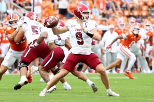 The cover for this Thursday night college football article shows Goose Crowder #9 of the Troy Trojans attempting to throw a pass during the first quarter against the Clemson Tigers.