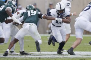 The article for this college football picks week 13 article shows Kaytron Allen #13 of the Penn State Nittany Lions breaking through the line past Armorion Smith #19 of the Michigan State Spartans