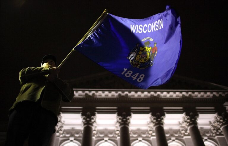 A protestor waves the Wisconsin state flag outside of the Wisconsin State Capitol.
