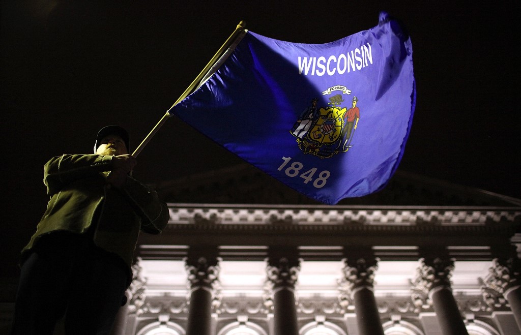 A protestor waves the Wisconsin state flag outside of the Wisconsin State Capitol.