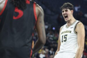 The cover for this college basketball picks today article shows Aday Mara #15 of the Michigan Wolverines yelling after making a basket against the San Diego State Aztecs