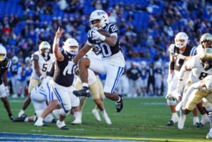 The cover for this college football picks week 15 article shows running back Nate Sheppard #20 of the Duke Blue Devils celebrating after scoring a touchdown against the Wake Forest Demon Deacons.