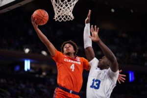 The cover for this college basketball picks today article shows Butta Johnson #4 of the Clemson Tigers going to the basket as Keba Keita #13 of the BYU Cougars defends.