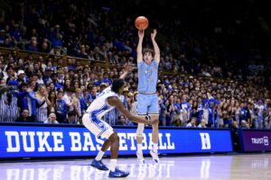 The cover for this college basketball picks today article shows Camp Wagner #8 of the Indiana State Sycamores taking a three-point shot against Dame Sarr #7 of the Duke Blue Devils.