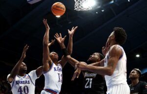 The cover for this college basketball picks today article shows Elmarko Jackson #13 and Flory Bidunga #40 of the Kansas Jayhawks competing with Jack Doumbia Jr. #21 of the Towson Tigers for a rebound.