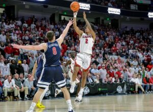 The cover for this college basketball picks today article shows Aden Holloway #2 of the Alabama Crimson Tide shooting a first-half shot over Ivan Kharchenkov #8 of the Arizona Wildcats during the C.M. Newton Classic.