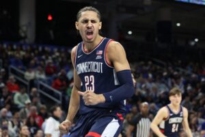 The cover for this college basketball picks article shows Jayden Ross #23 of the UConn Huskies celebrating a dunk during the second half against the DePaul Blue Demons.