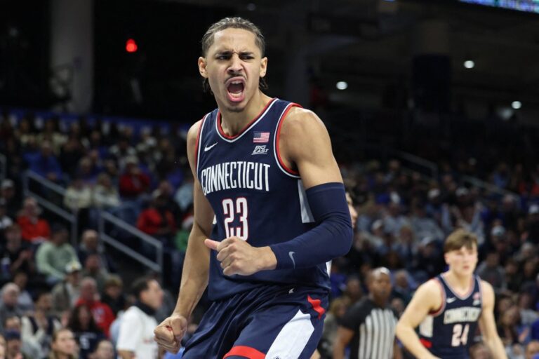 The cover for this college basketball picks article shows Jayden Ross #23 of the UConn Huskies celebrating a dunk during the second half against the DePaul Blue Demons.