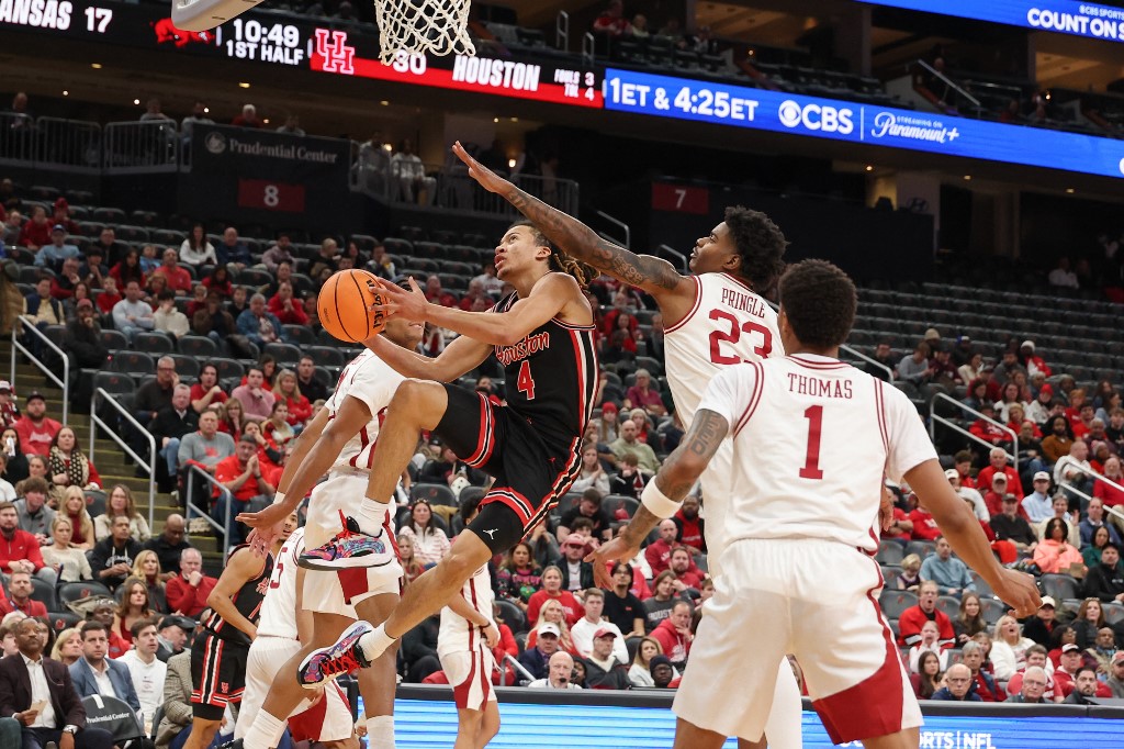 The cover for this college basketball picks today article shows Kingston Flemings #4 of the Houston Cougars shooting the ball as Nick Pringle #23 of the Arkansas Razorbacks defends.