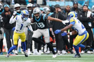 Jalen Coker #18 of the Carolina Panthers carries the ball between Emmanuel Forbes Jr. #1 and Kamren Kinchens #26 of the Los Angeles Rams.