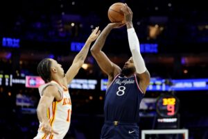 The cover for this NBA player props today article shows Paul George #8 of the Philadelphia 76ers shooting a three-pointer against Zaccharie Risacher #10 of the Atlanta Hawks.