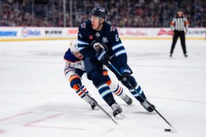 The cover for this NHL picks today article shows Logan Stanley #64 of the Winnipeg Jets skating with the puck in the second period against the Edmonton Oilers.