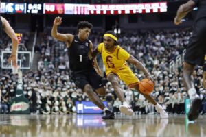 The cover for this college basketball picks today article shows Kam Woods #13 of the USC Trojans driving to the basket against Jeremy Fears Jr. #1 of the Michigan State Spartans.