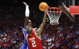 The cover for this college basketball picks today article shows Keba Keita #13 of the Brigham Young Cougars flying to block a shot by Terrence Brown #2 of the Utah Utes.