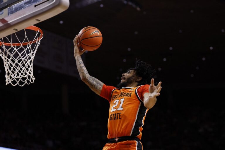 The cover for this college basketball picks today article shows Isaiah Coleman #21 of the Oklahoma State Cowboys laying up a shot as in the second half of play against the Iowa State Cyclones.