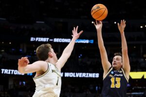 The cover for this college basketball picks today article shows Tyler McGhie #13 of the UC San Diego Tritons shooting against Danny Wolf #1 of the Michigan Wolverines during the second half in the first round of the NCAA Men's Basketball Tournament.
