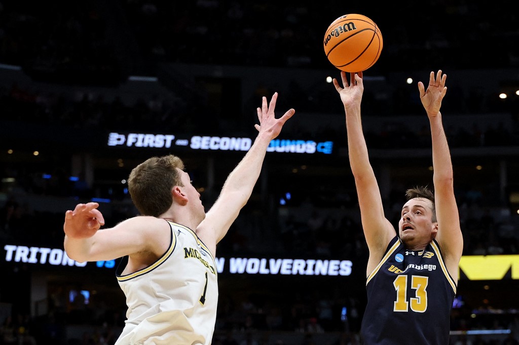 The cover for this college basketball picks today article shows Tyler McGhie #13 of the UC San Diego Tritons shooting against Danny Wolf #1 of the Michigan Wolverines during the second half in the first round of the NCAA Men's Basketball Tournament.