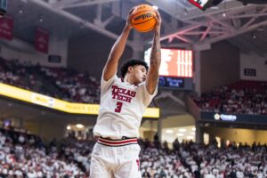 The cover for this college basketball picks today article shows LeJuan Watts #3 of the Texas Tech Red Raiders rebounding the ball during the first half of the game against the Kansas Jayhawks.